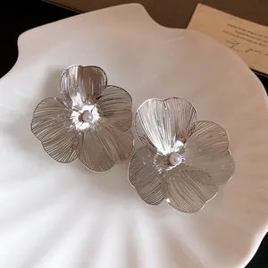 Detailed view of silver wire-drawn flower earrings with pearl centers on a shell tray