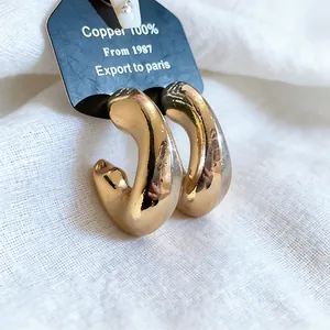 Detailed macro shot of chunky gold C-shaped hoop earrings on white textured linen fabric