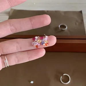 Macro detail view of colorful zircon cluster stud earrings held between fingers for scale