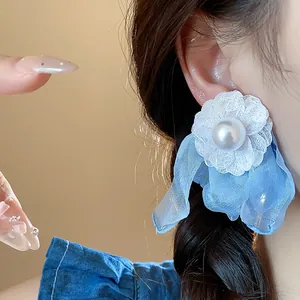 Detail view of white chiffon flower earring with blue fabric and central pearl