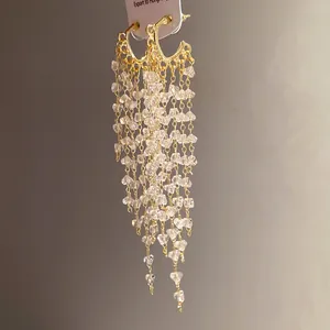 Vue détaillée des boucles d'oreilles en C dorées avec de longs glands en cristal.