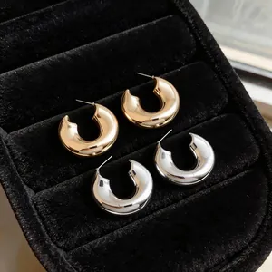 Macro view of minimalist gold and silver chunky C-shaped hoop earrings in black jewelry tray