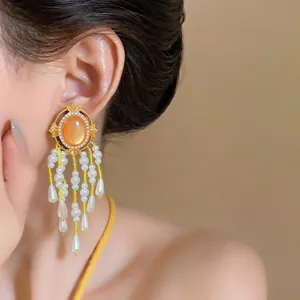 Nahaufnahme goldene Ohrhänger im Vintage-Stil mit orangefarbenem Stein und Perlenfransen