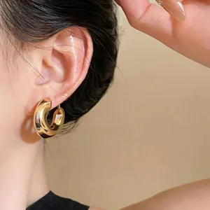 Close-up view of minimalist chunky gold C-shaped hoop earrings on a female model's ear