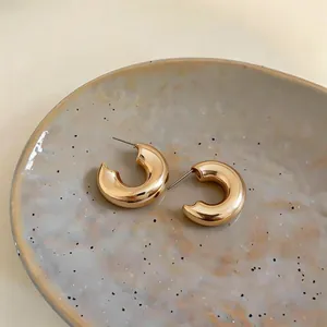Detailed view of chunky gold metallic C-shaped hoop earrings on ceramic dish