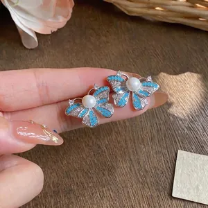 Elegant silver butterfly stud earrings with blue accents and white pearls on a hand