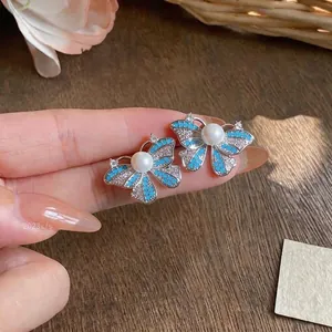 Close-up detail of blue enamel butterfly stud earrings with pearl and sparkling zircons