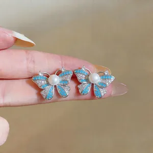 Close-up of butterfly stud earrings with blue wings and a central pearl detail