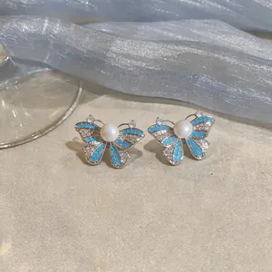 Macro detail of elegant butterfly stud earrings with blue enamel and pearl center