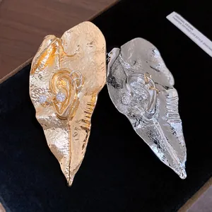 Dettaglio di spille a foglia martellata con design a orecchio e cristalli.