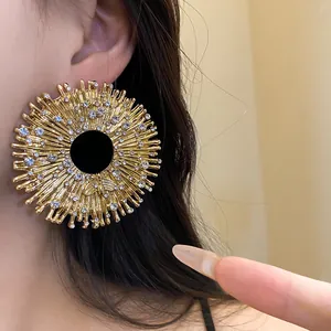 Close-up of a large gold sunburst earring featuring a small bee and rhinestones on model