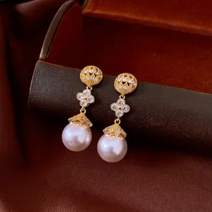 Macro detail of gold-plated pearl earrings with elegant sparkling lucky flower accents.