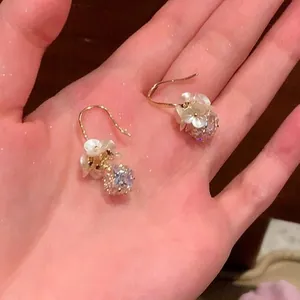 Elegant floral pearl and crystal ball drop earrings with gold hooks displayed on a hand