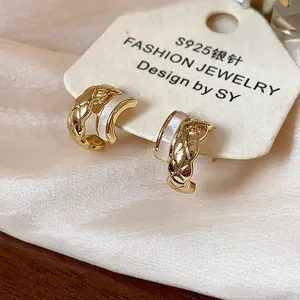 Detail of gold-plated C-shaped stud earrings with lattice pattern and white inlay.