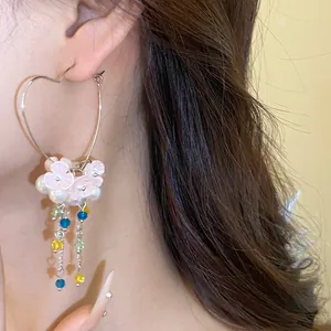 Close-up of heart hoop earring with pearl flowers and colorful beaded tassels details.