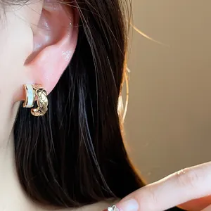 Close-up of 18k gold-plated C-shaped earring with quilted pattern and white enamel