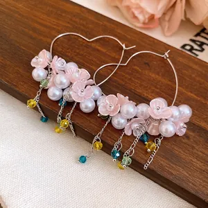 Detailed view of handmade pearl flower tassel heart-shaped earrings on a rustic wood stand