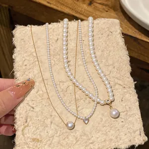 Three elegant 14k gold plated pearl necklaces with heart and eye pendants on textured board