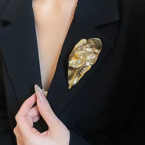 Dettaglio macro di una spilla dorata a forma di foglia su un blazer nero elegante
