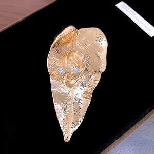 Dettaglio macro di una spilla a foglia dorata con design a orecchio e cristalli