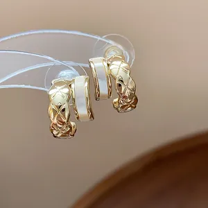 Detail of gold-plated quilted C-shaped hoop earrings with elegant white inlay texture