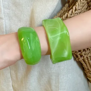 Dettaglio macro di bracciali geometrici in acrilico marmorizzato verde su polso donna