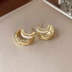 Close-up of 18k gold plated C-shape earrings with quilted texture and white inlay