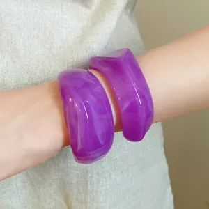 Primo piano dettagliato di bracciali geometrici in acrilico marmorizzato viola sul braccio.