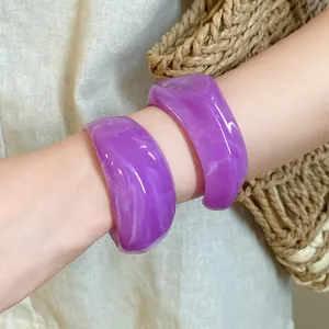 Dettaglio macro di due bracciali rigidi in acrilico viola marmorizzato su un polso