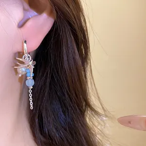 Primer plano de pendiente de golondrina plateado con perlas y cristales azules en oreja.