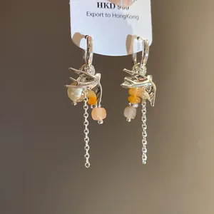 Primer plano de pendientes de aro de golondrina plateados con perlas y borlas.