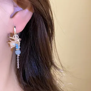 Detalle de pendiente de golondrina plateado con perla y borla de cristal azul en la oreja