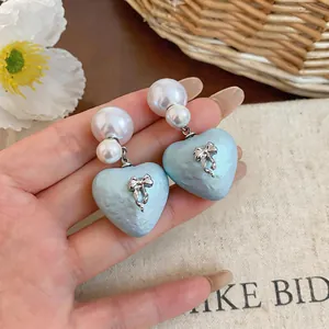 Close-up of light blue textured heart earrings with white pearls and bow detail.