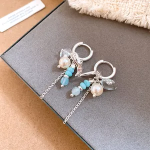 Primer plano de elegantes pendientes de aro plateados con golondrinas y perlas