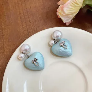 Detailed view of elegant light blue heart stud earrings featuring pearls and silver bows.