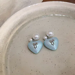 Close-up view of elegant heart-shaped pearl earrings with silver bow details on a dish