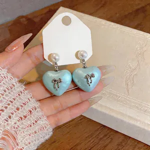 Close-up of light blue heart-shaped pearl earrings with silver bow details