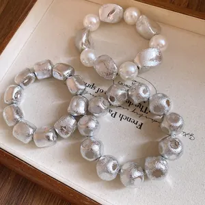 Detailed view of vintage irregular silver beads and pearl bracelets on a cream fabric tray.