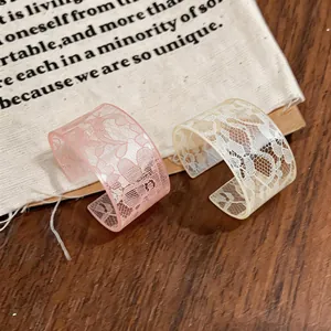 Close-up of acrylic cuff bracelets with delicate white lace patterns in pink and cream.
