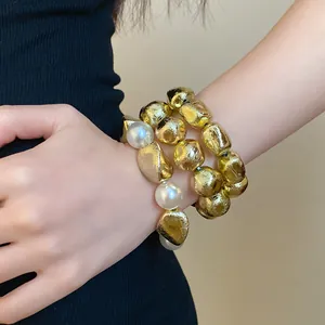 Detailed view of irregular gold beads and white pearl bracelets on a model's wrist.