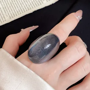 Detail view of a large, irregular dark blue resin ring on a finger with manicured nails