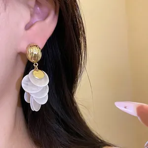 Elegant 14k gold plated shell round tassel earrings shown worn on an ear of a model