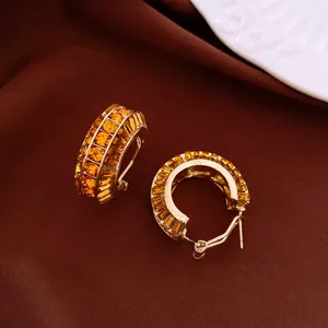 Dettaglio di eleganti orecchini a cerchio dorati con cristalli ambrati scintillanti