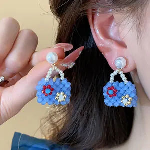 Close-up of blue beaded bag earrings with pearl studs worn on a model ear, detailed view.
