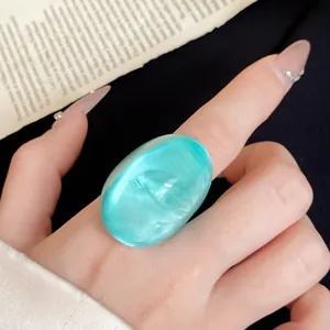 Close-up of an irregular turquoise resin ring with a pearlescent finish on a finger.