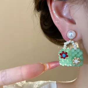 Macro detail of whimsical green beaded handbag earrings with pearl studs worn on ear