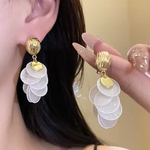 Detailed close-up of gold-plated tassel earrings with layered white shell discs on model