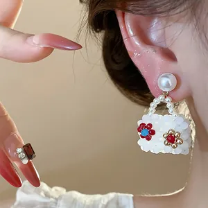 Detailed view of a white beaded handbag-shaped earring with pearl and floral accents