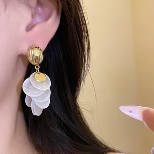 Detailed shot of 14k gold-plated circular shell tassel drop earrings on model's ear
