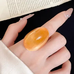 Detailed view of a chunky oval orange resin ring featuring a translucent cat-eye finish.